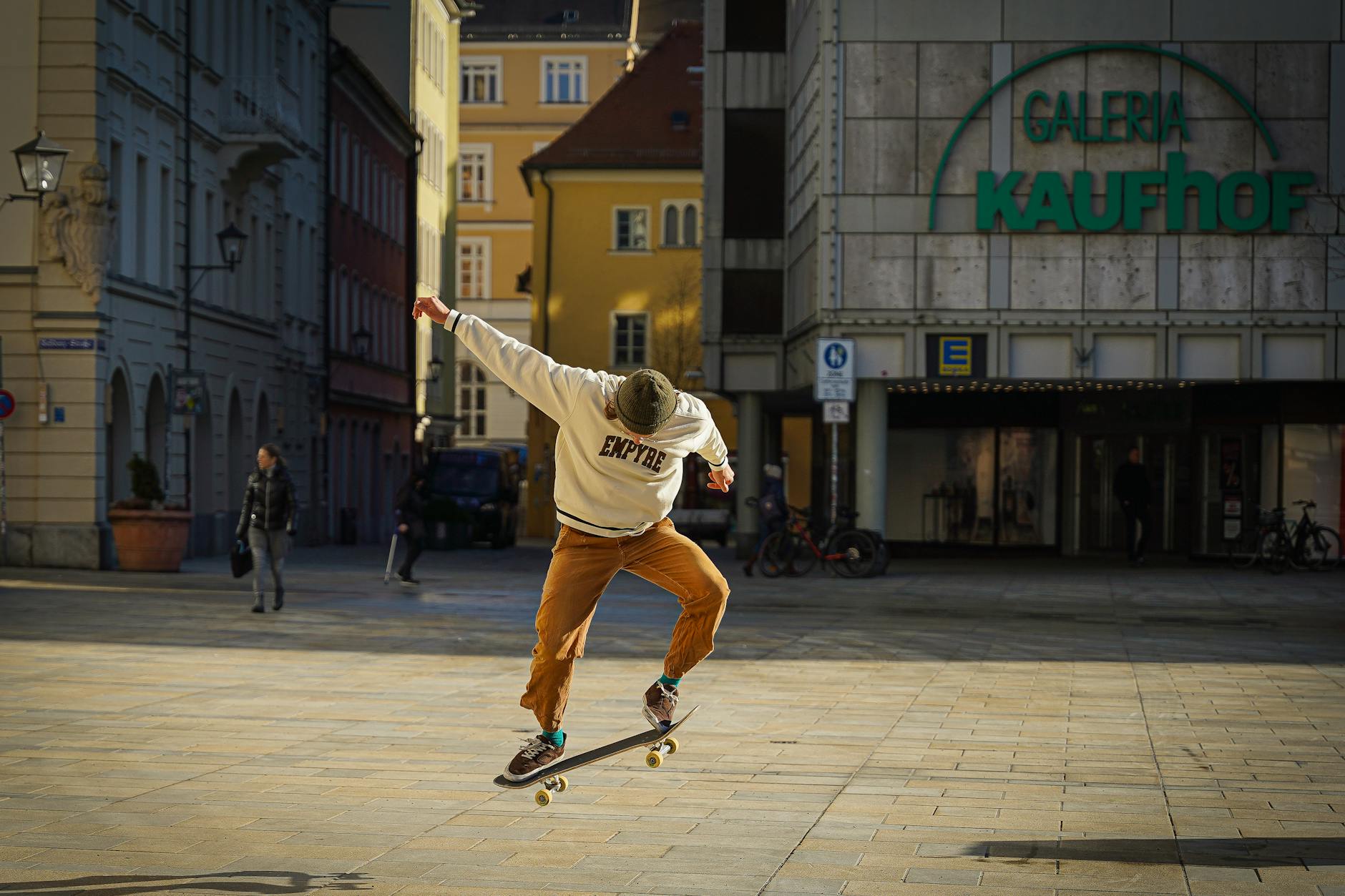 Skateboarder performing a trick in a lively urban square with buildings.